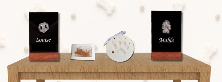 Four pet keepsakes on a table, including a clipping of fur and a paw print ornament