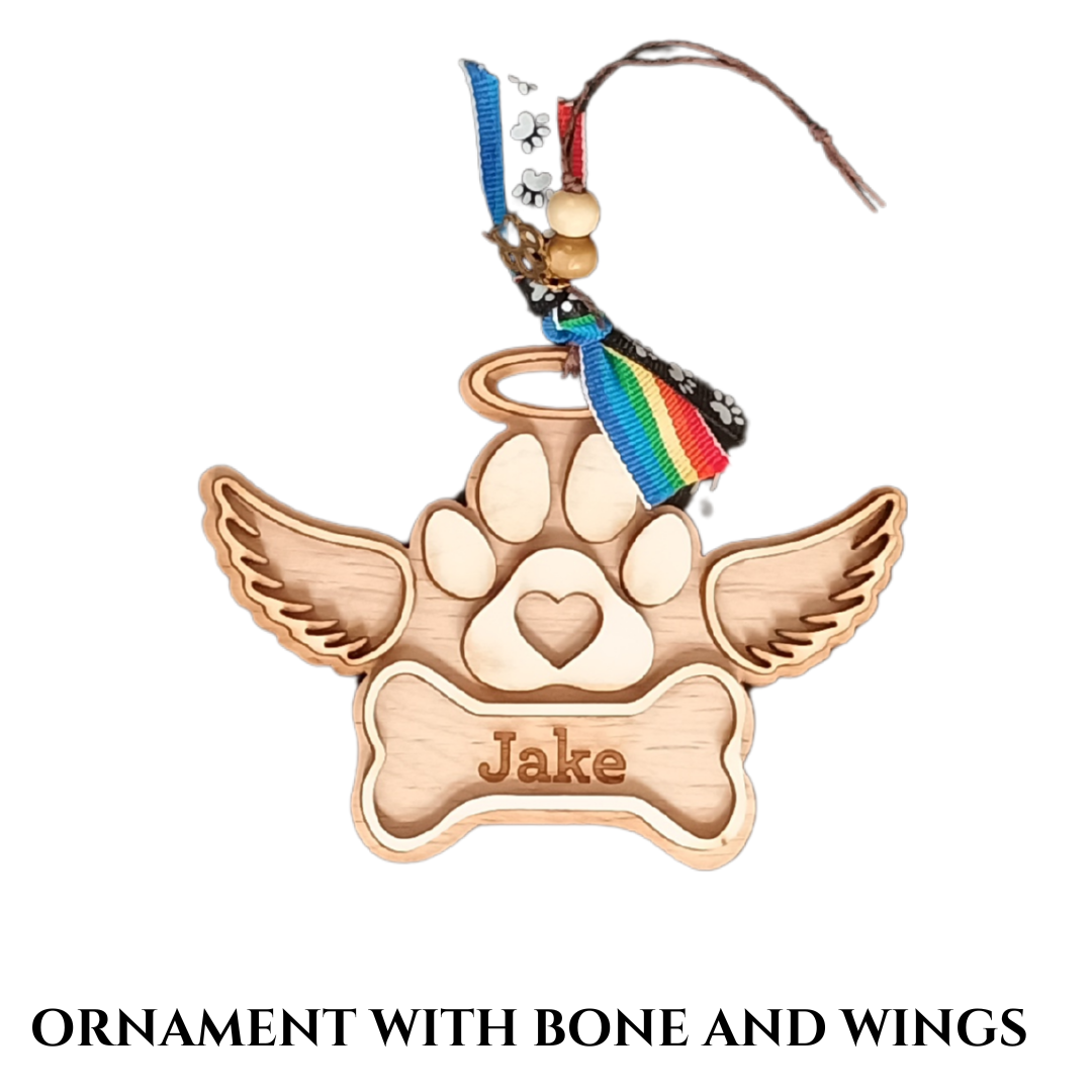 Small, wood heart-shaped ornament with a paw print, bone, and wings, and a dog's name engraved on the bone.
