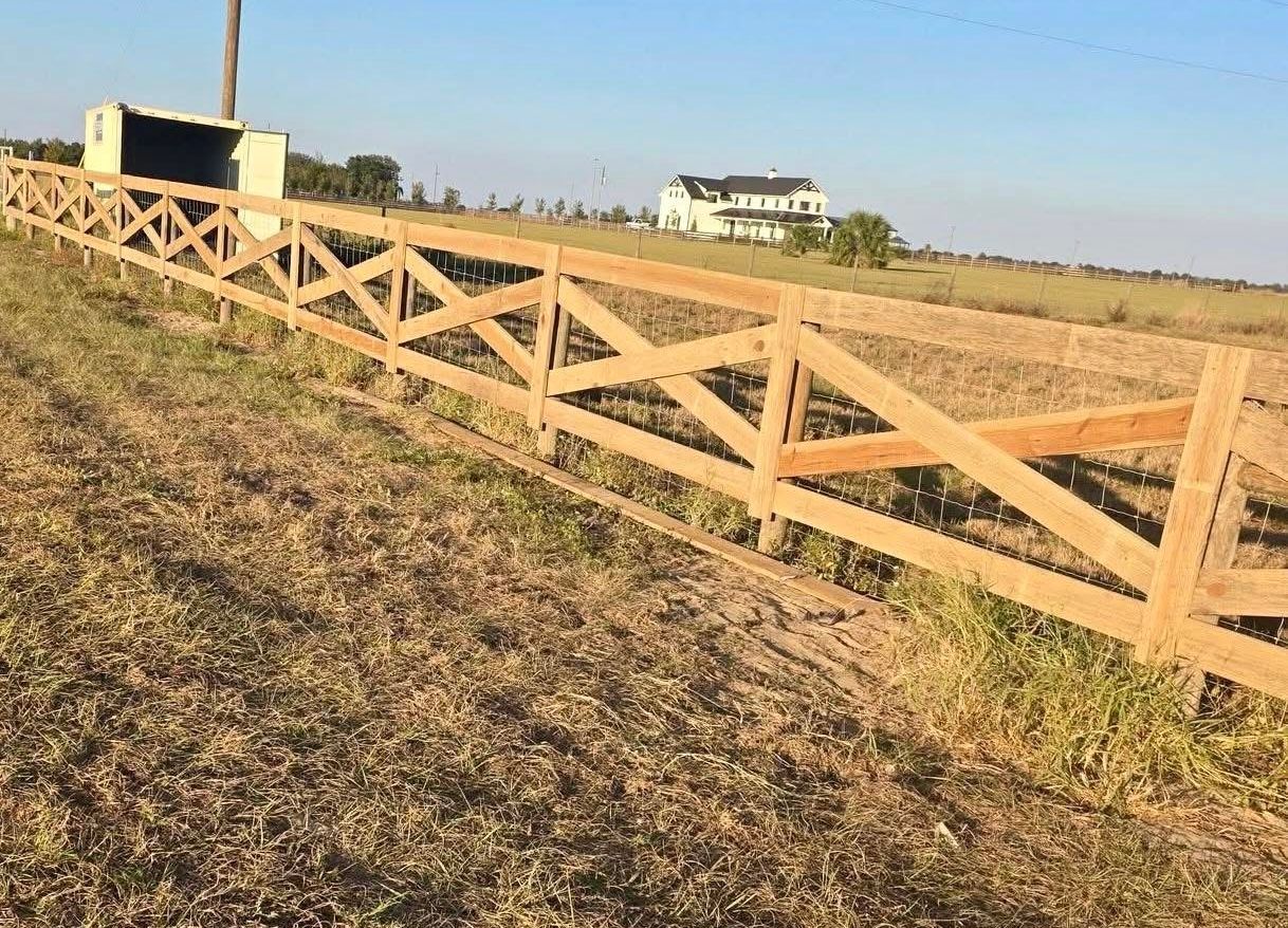 Wooden fence along a dry field with a white house in the distance under a clear blue sky
