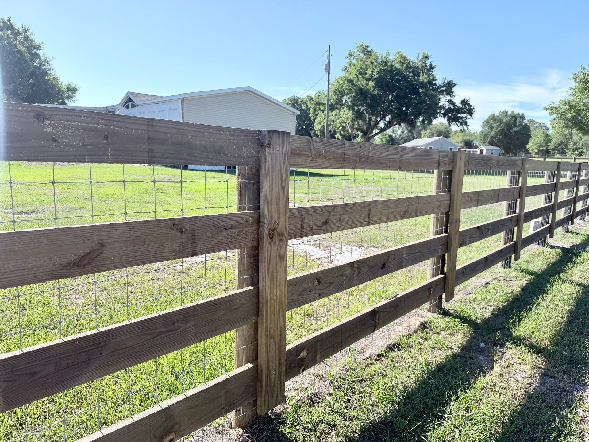 Wooden ranch fence beside a grassy field under a sunny blue sky