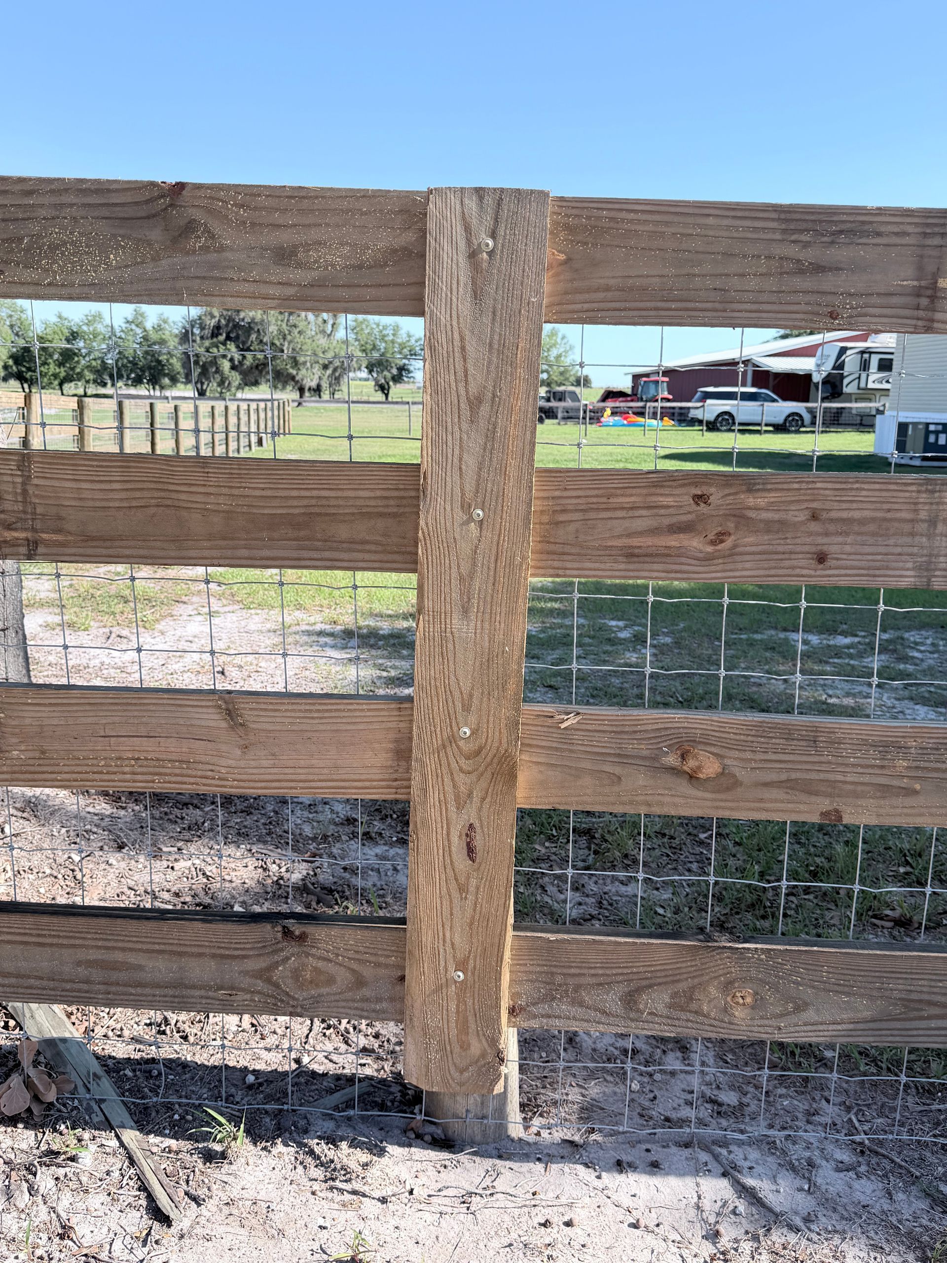 Wooden fence with three horizontal rails and a central post in a rural field