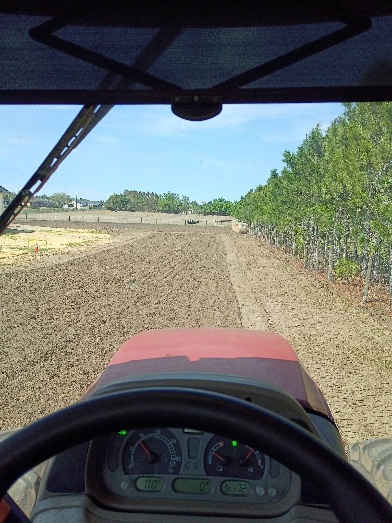View from a tractor driving over a dirt field beside green crops under a clear sky