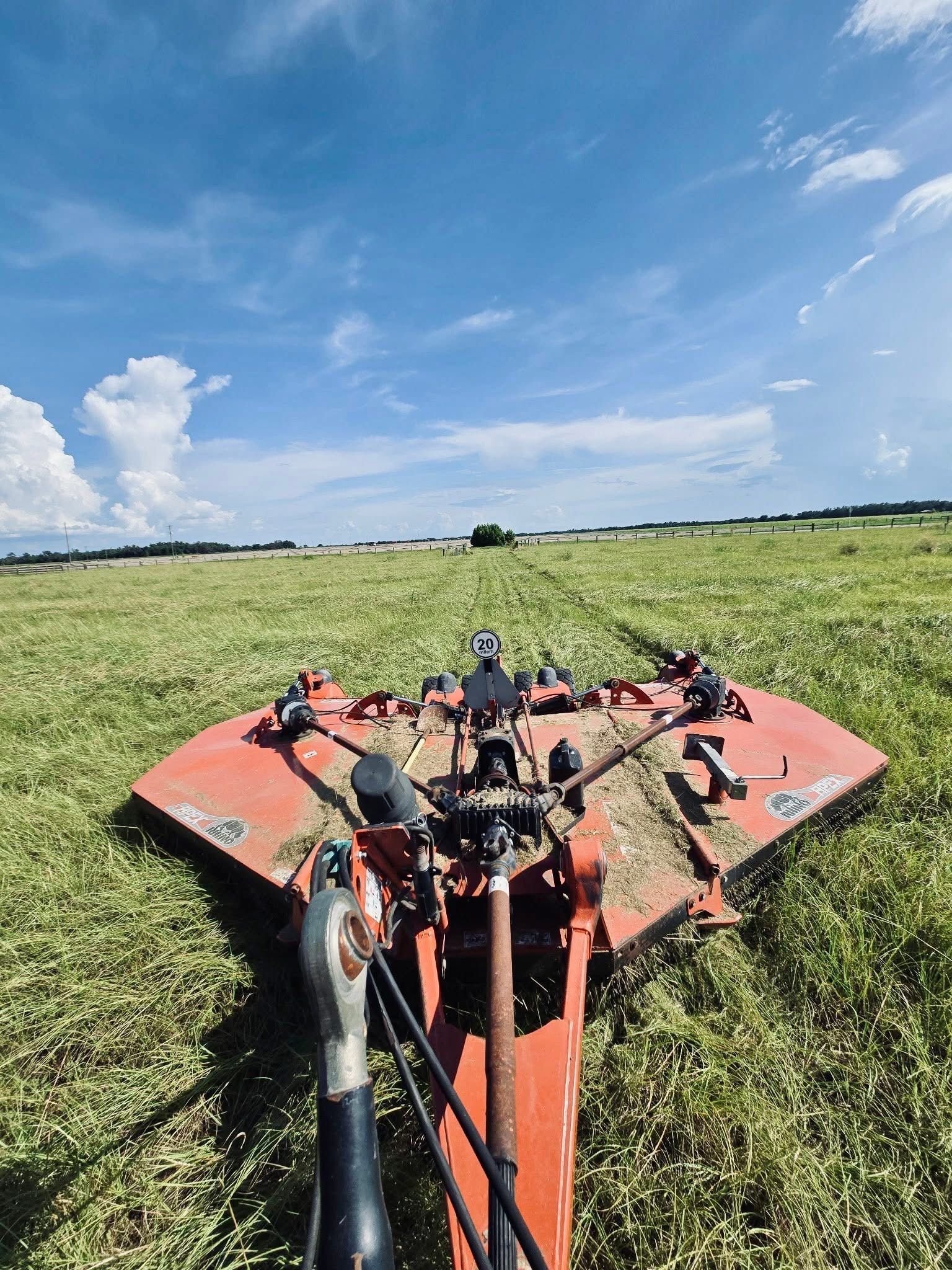 Person riding a red mower across a grassy field under a blue sky