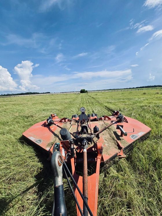 Person riding a red mower across a grassy field under a blue sky