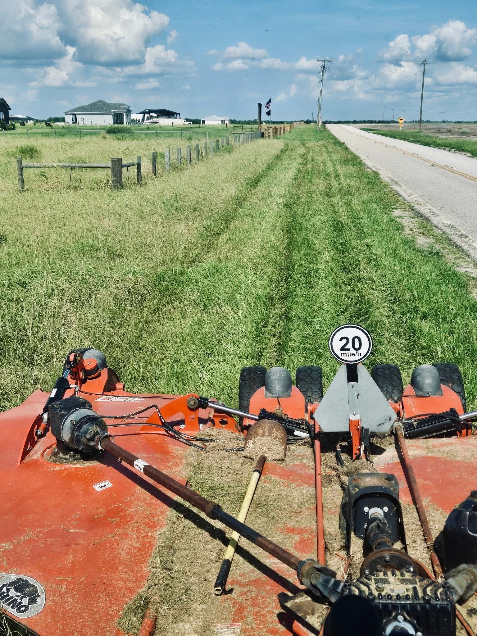 View from orange farm machinery on a rural roadside, with grassy fields and a 20 mph sign ahead.