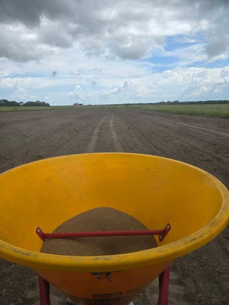 Yellow fertilizer spreader in a plowed field under a cloudy sky