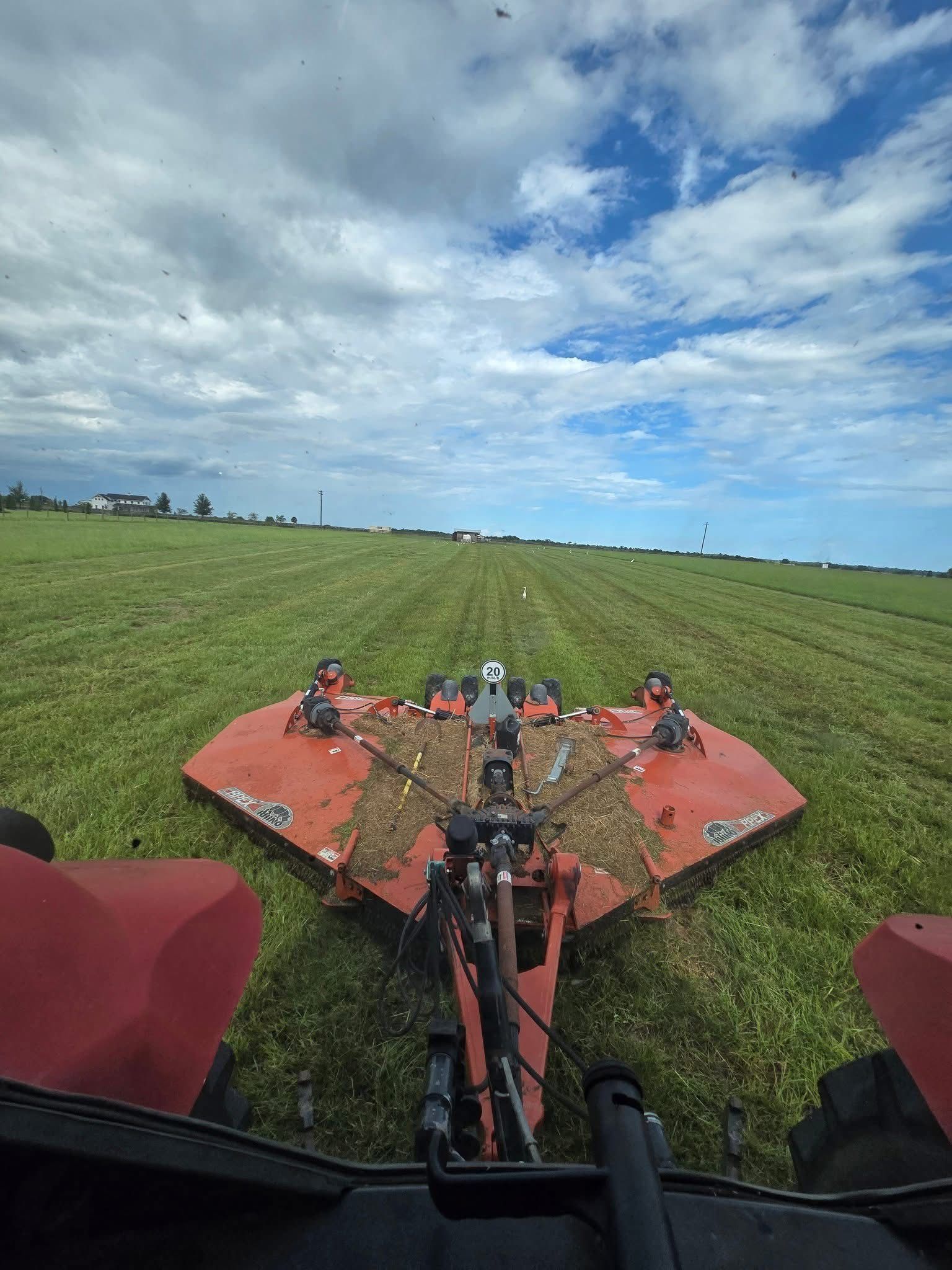 View from a tractor mowing a grassy field under a partly cloudy blue sky