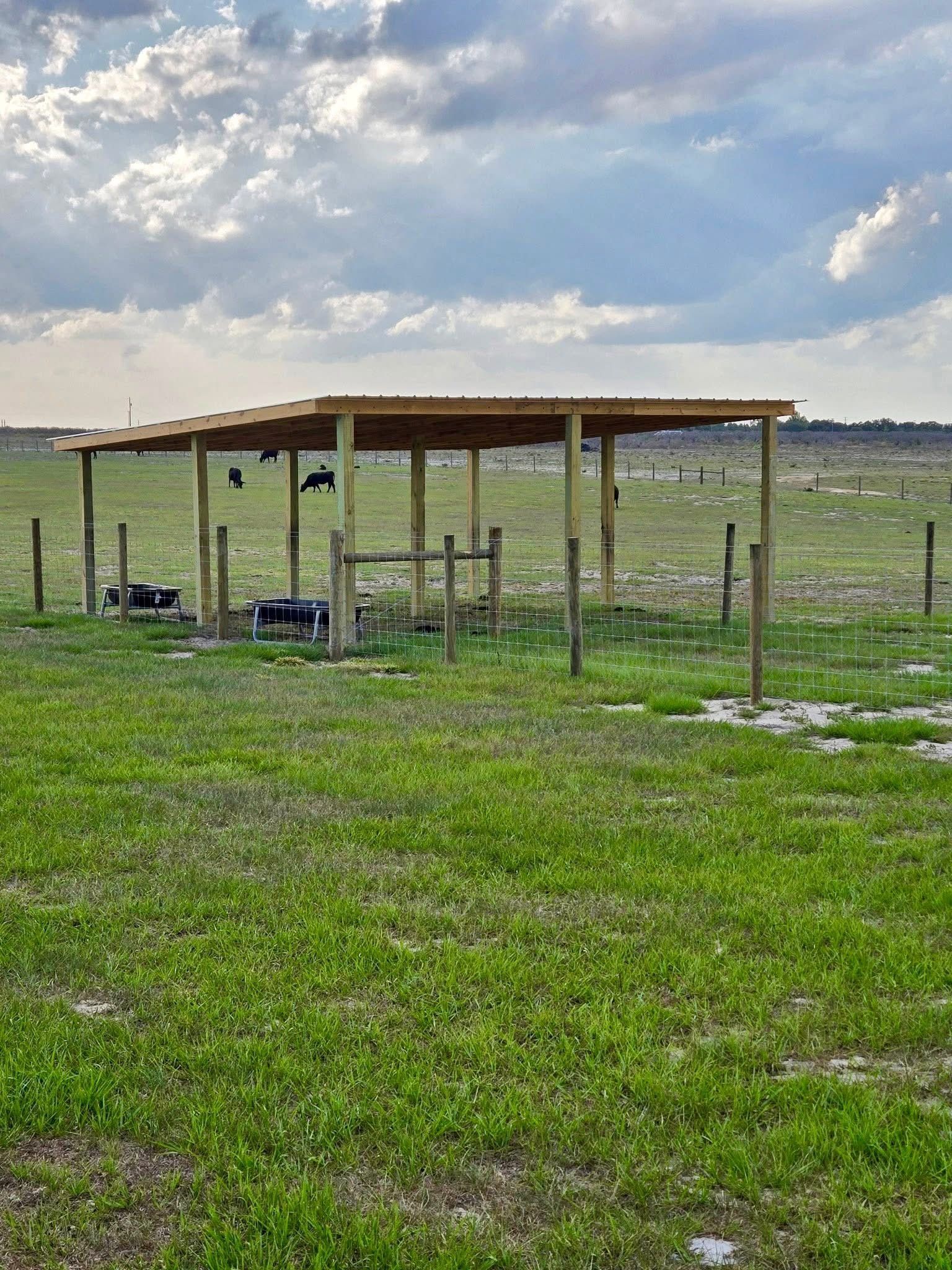 Small open-sided wooden shelter in a grassy field under a cloudy sky.