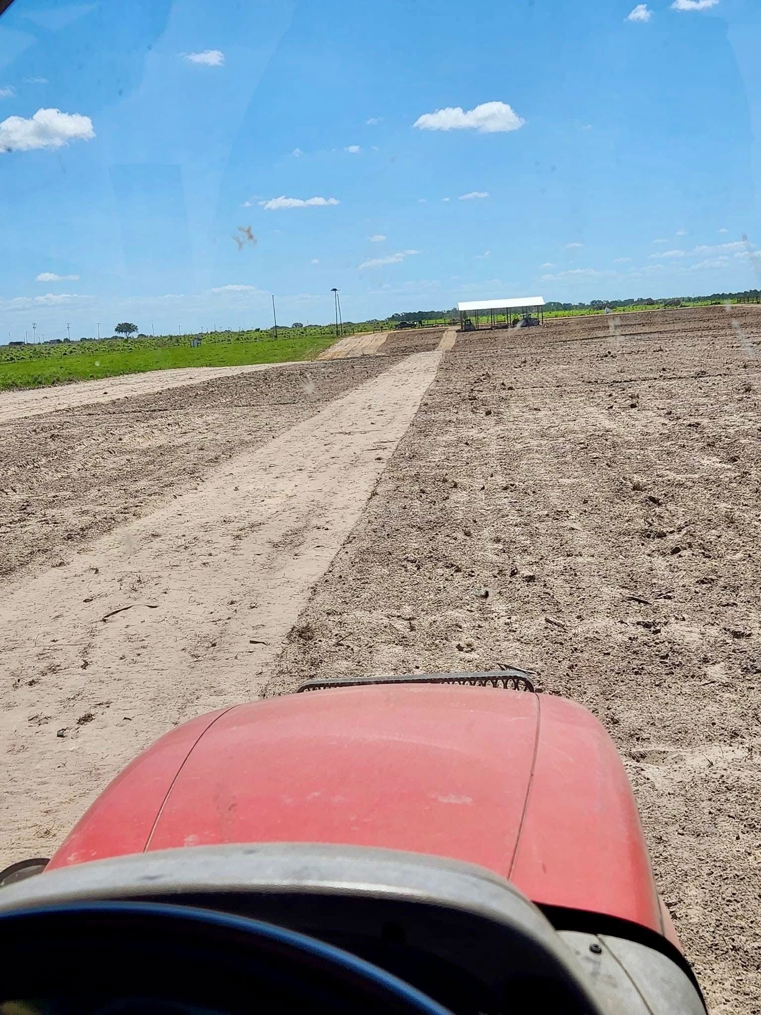 Red tractor hood in foreground on a dirt path through a plowed field under a blue sky