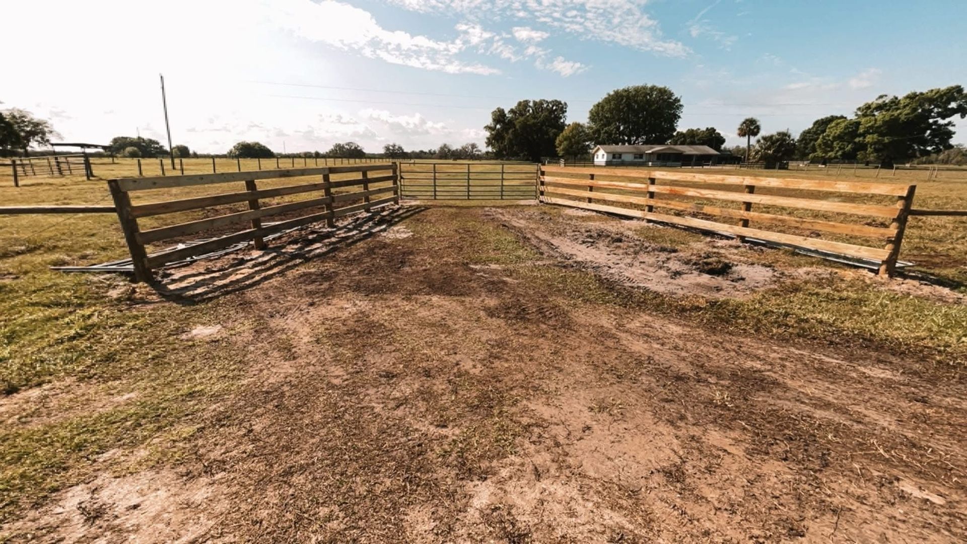 Dirt path between wooden livestock fences in a rural pasture under a bright sky