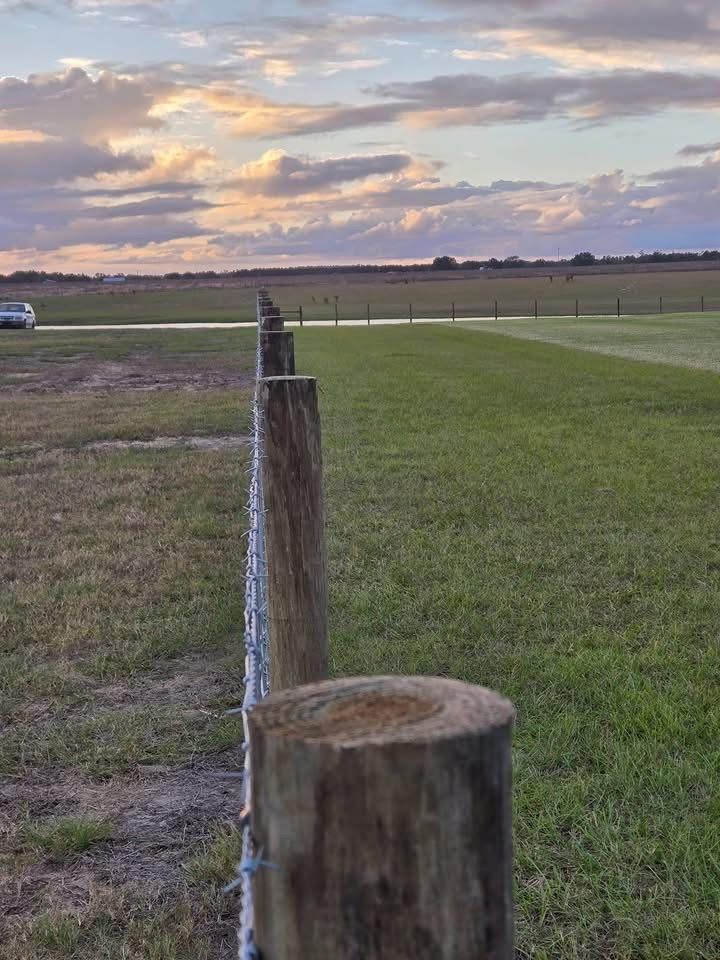 Weathered fence posts line a grassy field at sunset under a cloudy sky.