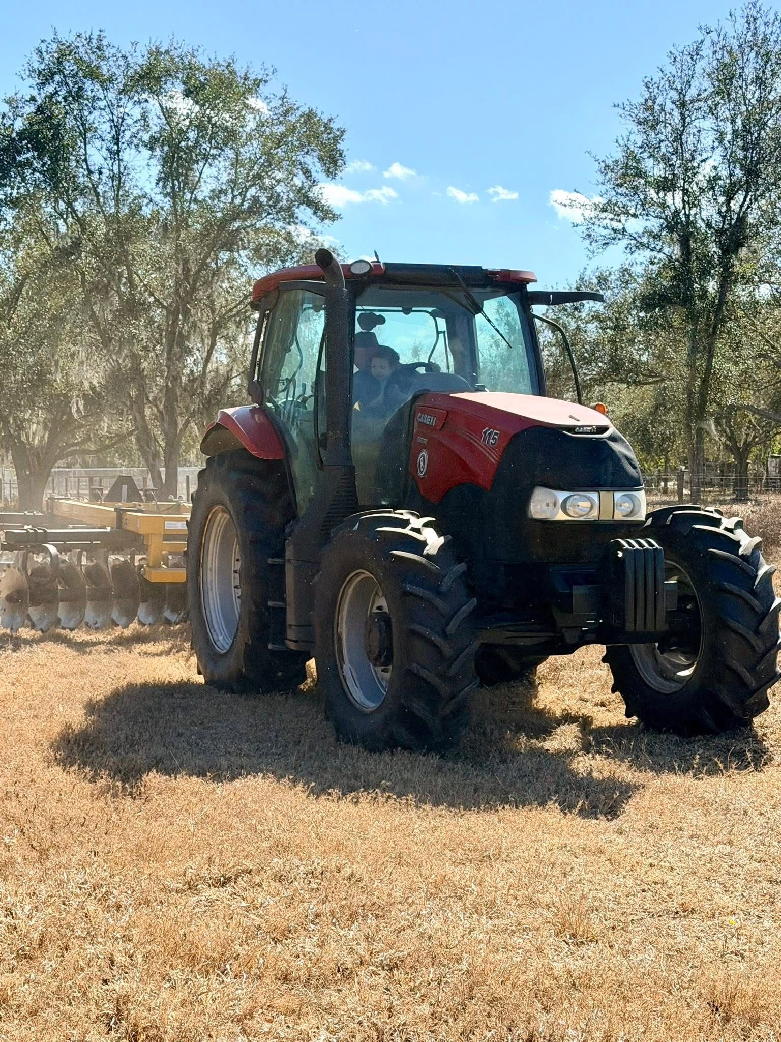 Red tractor in a dusty field among trees under a blue sky