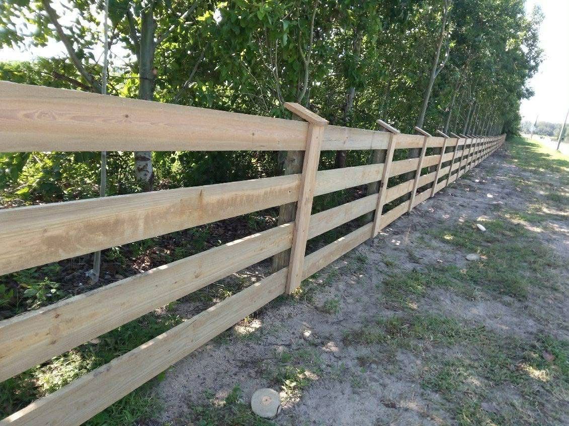 Long wooden fence along a gravel path beside green trees on a sunny day