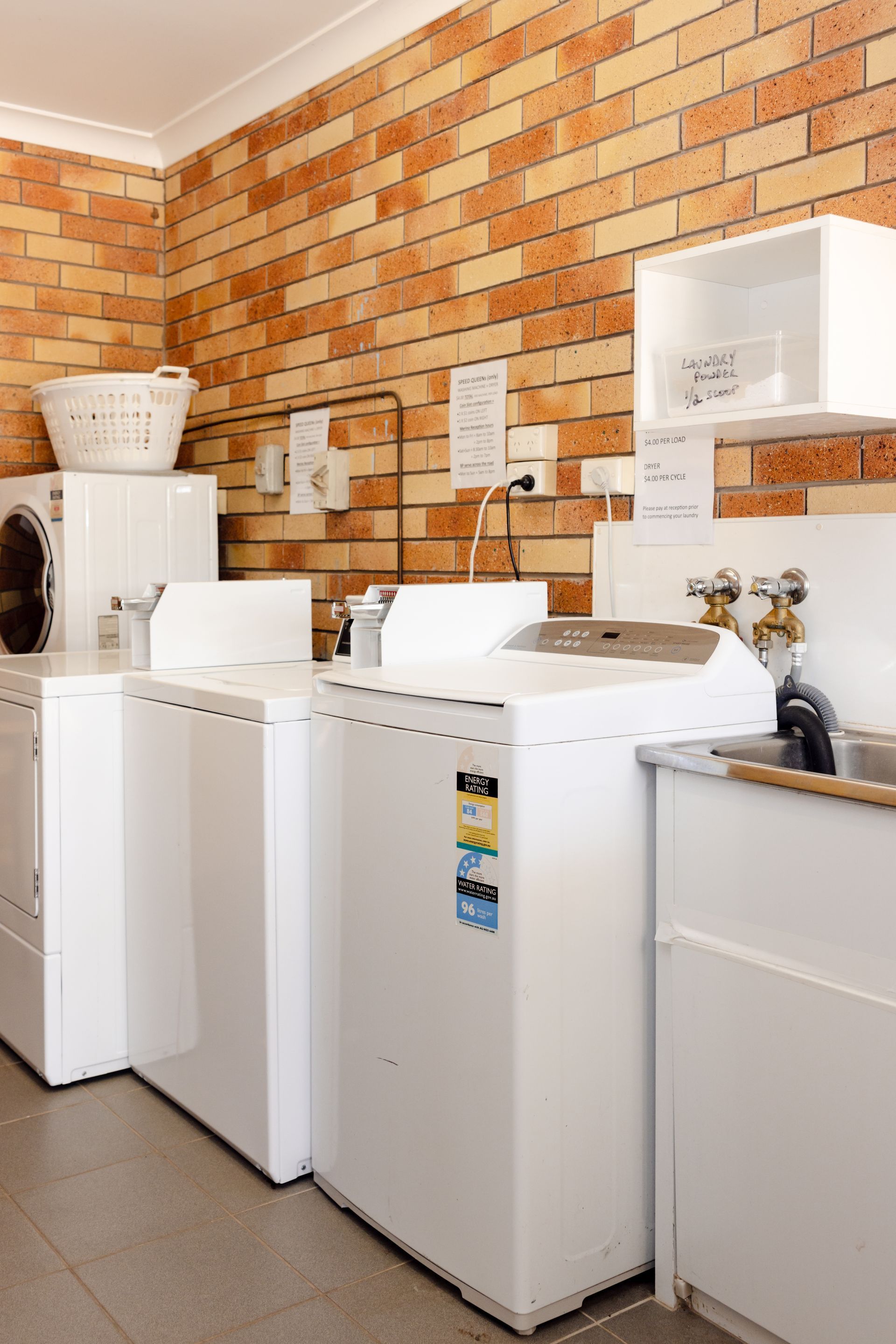 Laundry room with white washers and a dryer against a brick wall