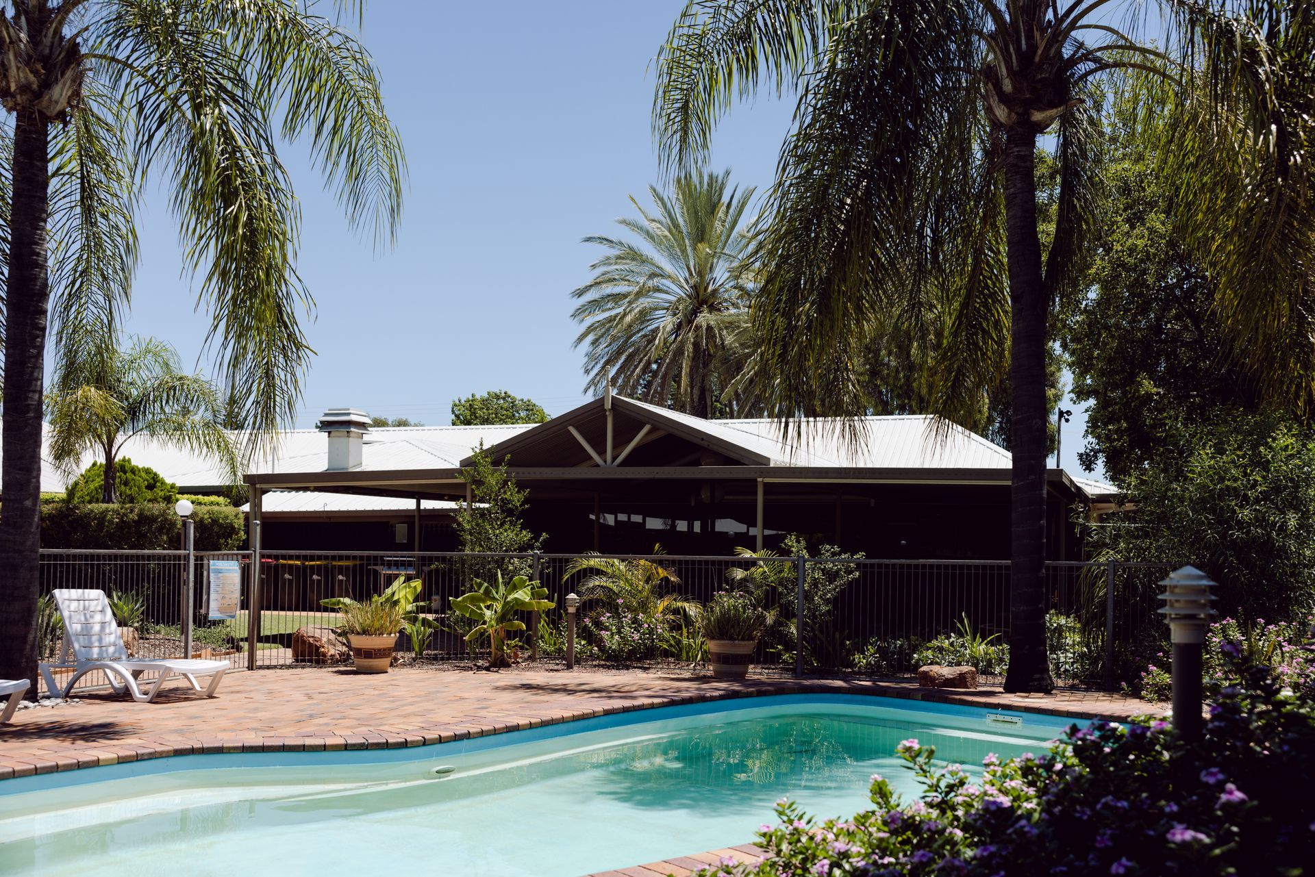 Motel pool with palm trees and a shaded patio beside a house