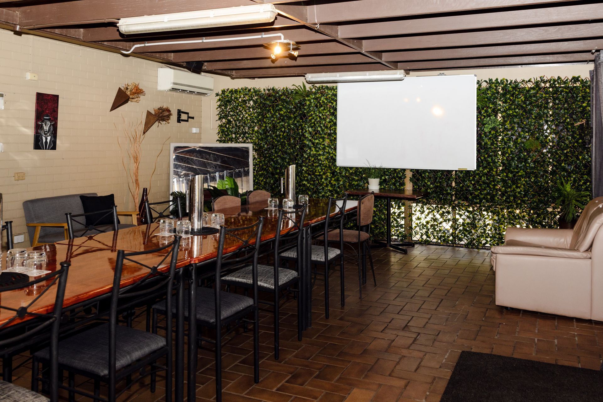 Indoor event room with long table, projector screen, brick floor, and green wall panels