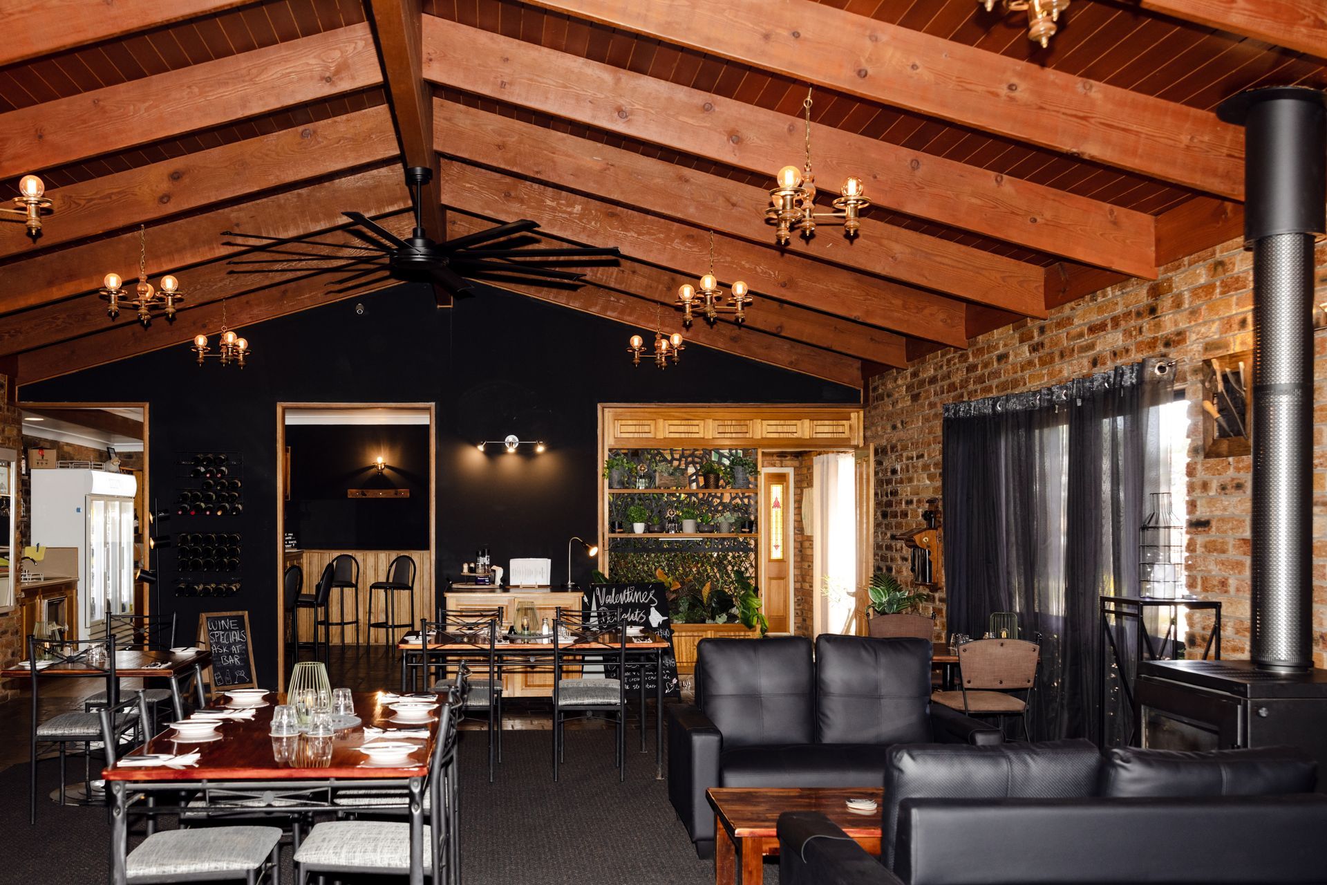 Rustic lodge lounge with wood-beamed ceiling, black leather sofas, tables, and a stone fireplace