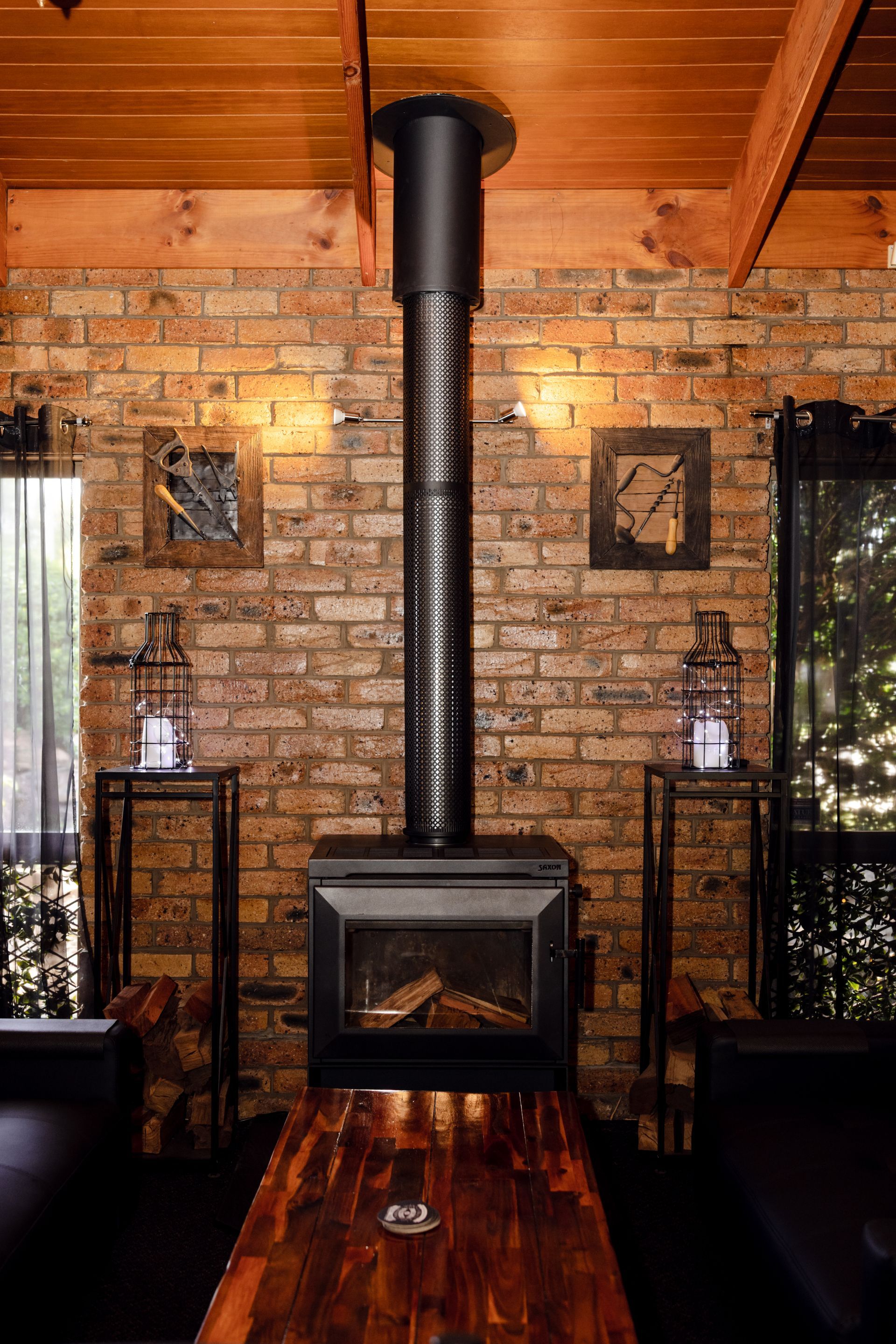 Cozy rustic room with brick walls, wood ceiling, and a black wood stove centered between two side tables.