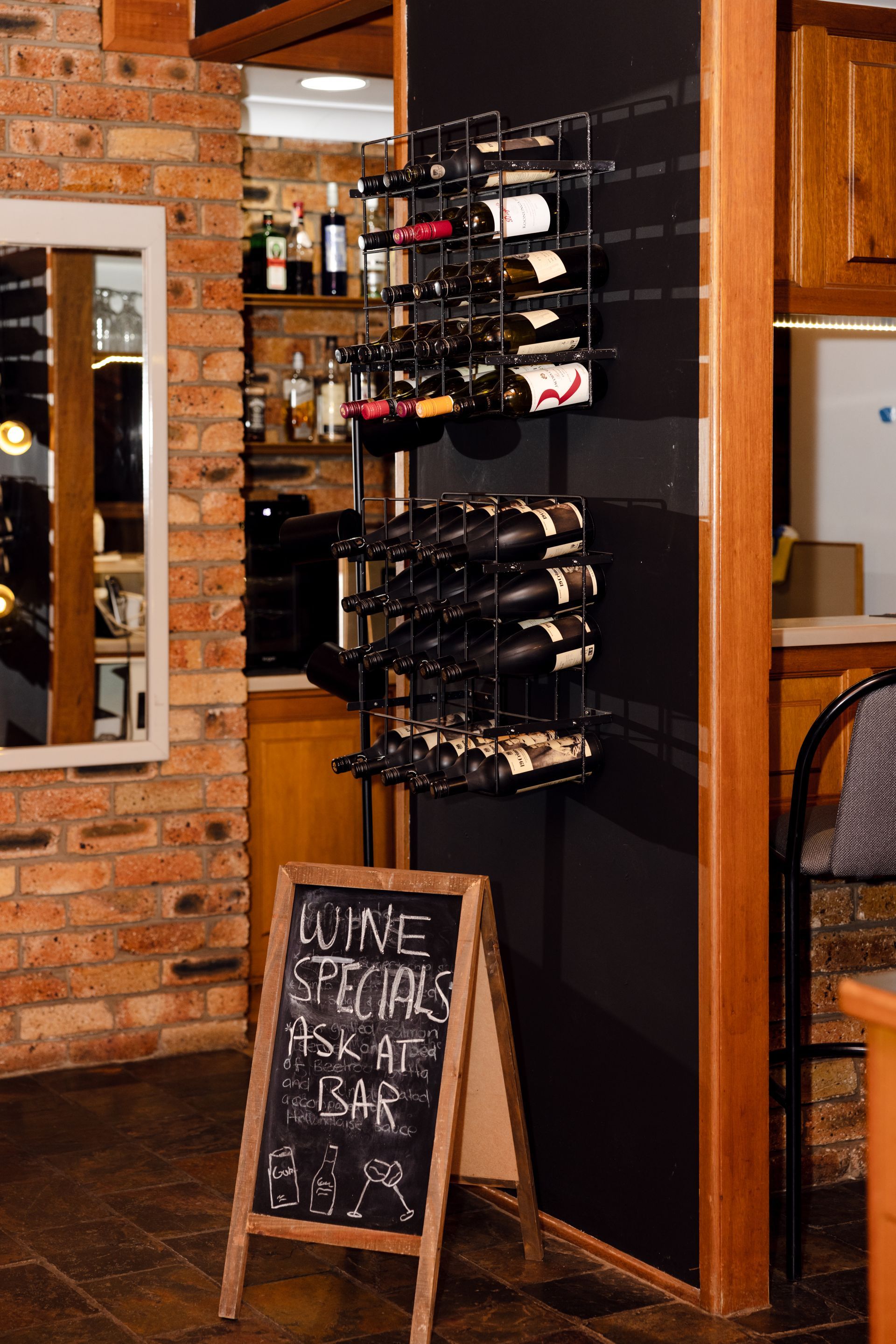 Wine bottles displayed on a rack beside a chalkboard sign in a rustic restaurant or bar entryway