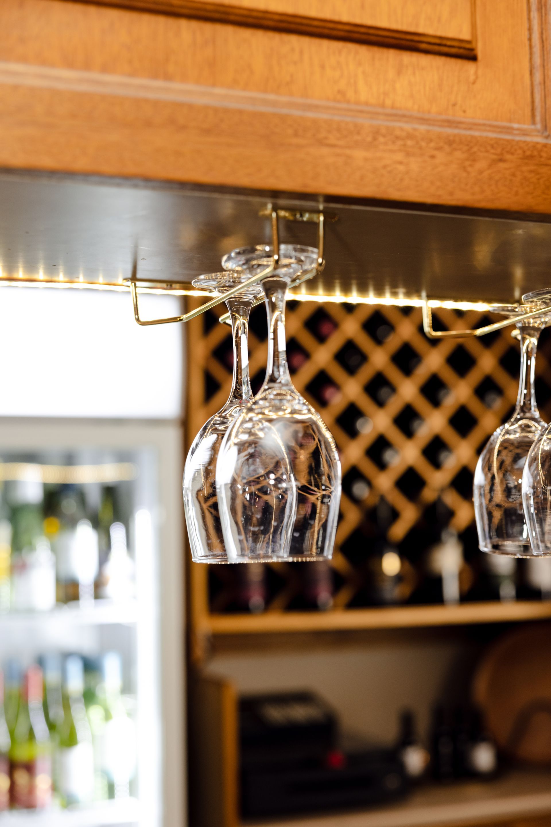 Wine glasses hanging under a wooden kitchen cabinet with a wine rack in the background