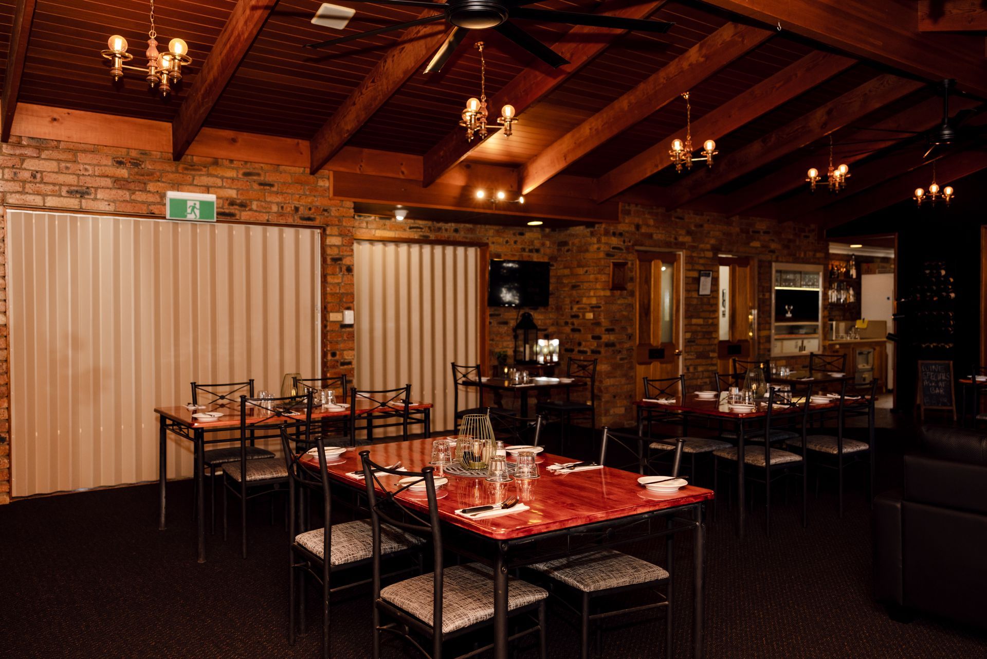 Warm restaurant dining room with red tablecloths, wooden ceiling, and dim chandelier lighting