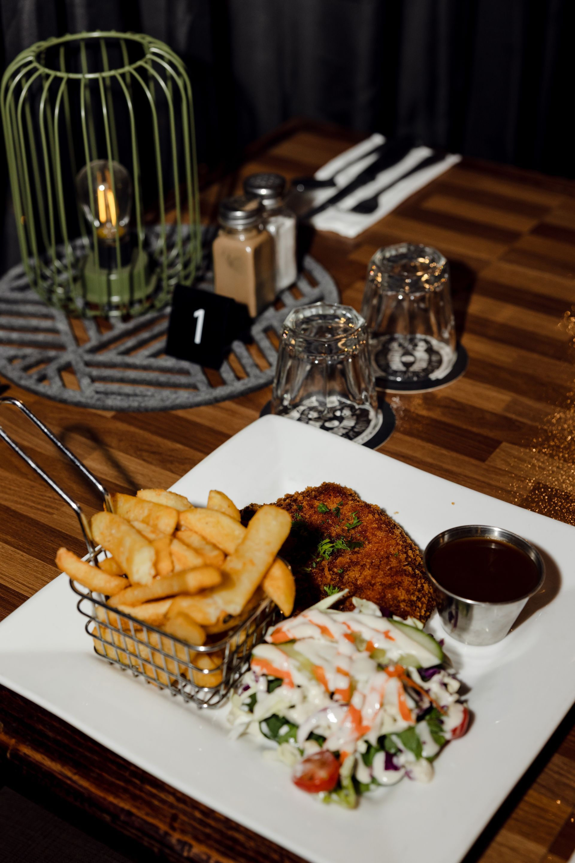 Plated meal with fries, salad, and steak on a checkered table beside utensils and glassware