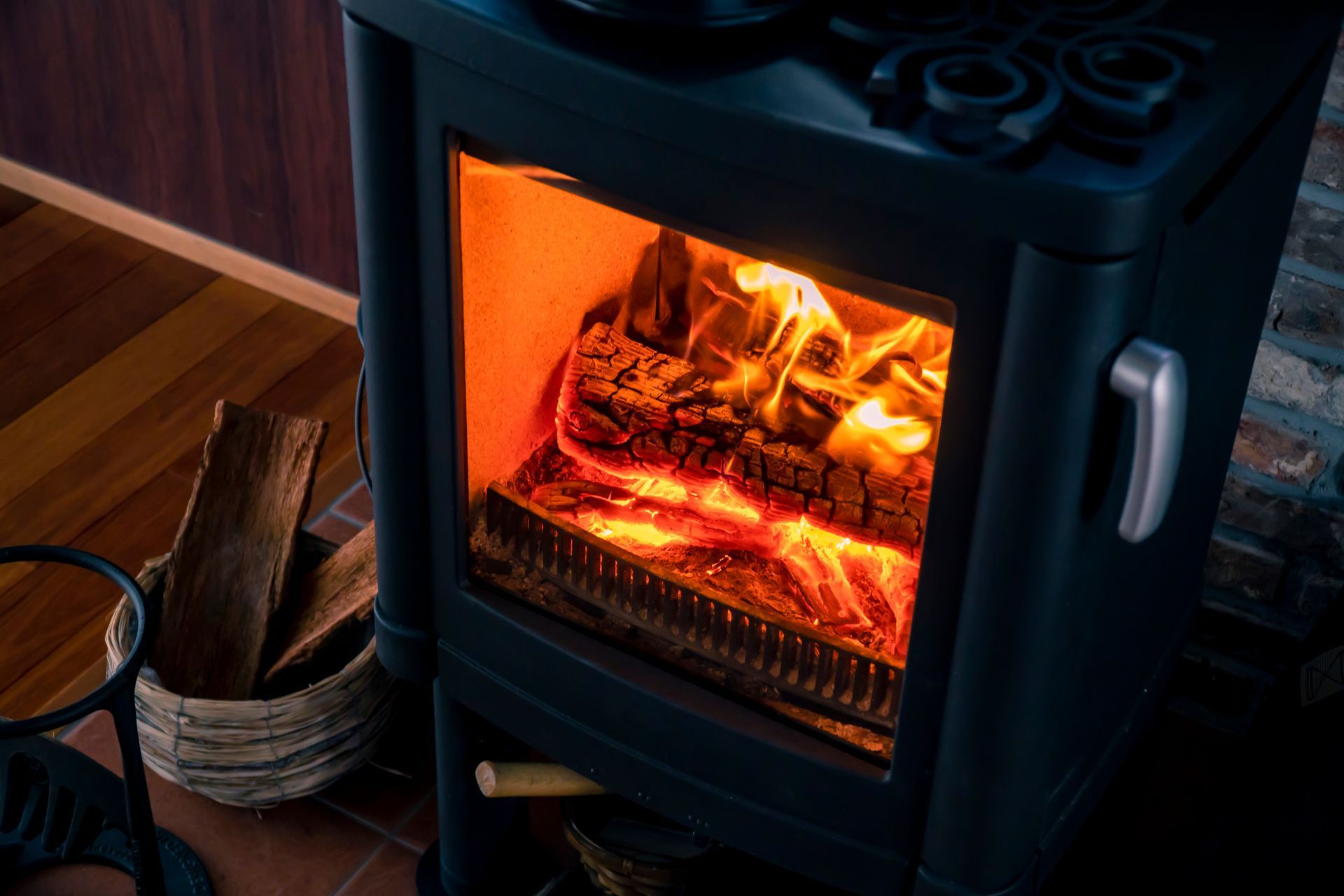 Black Wood Stove With Glowing Fire Beside a Basket of Firewood — Southern Trade Services in Hobart, TAS 