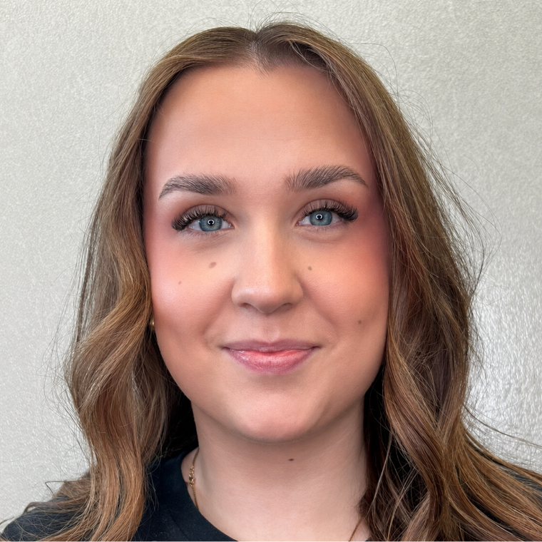 Portrait of a smiling person with wavy brown hair and blue eyes against a plain gray background