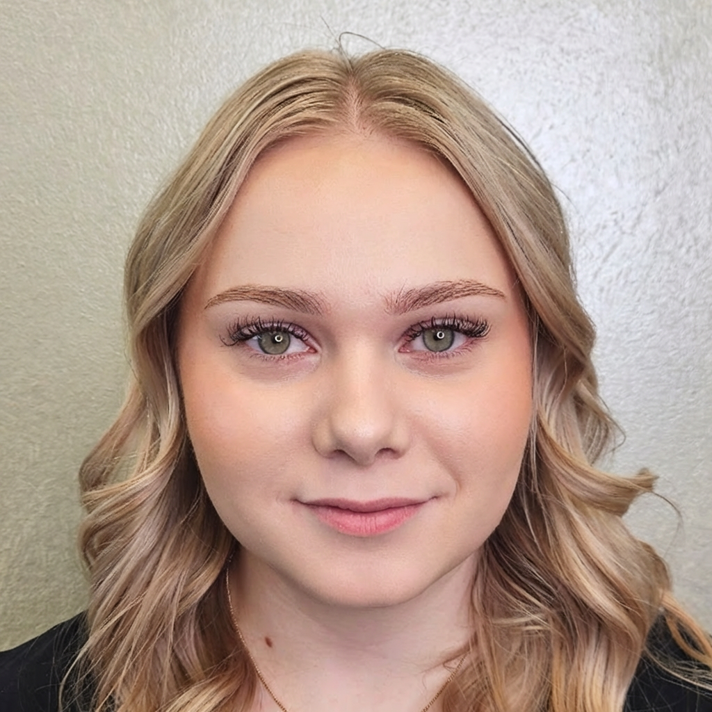 A person with shoulder-length blonde hair and a neutral expression centered against a light green wall.