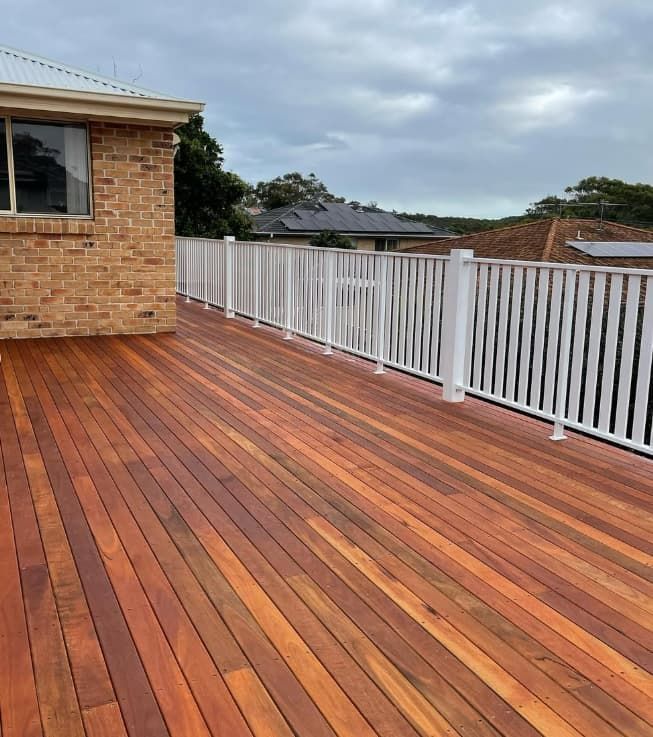 A Wooden Deck With A White Railing And A Brick Building In The Background — Penman Projects In Shoal Bay, NSW