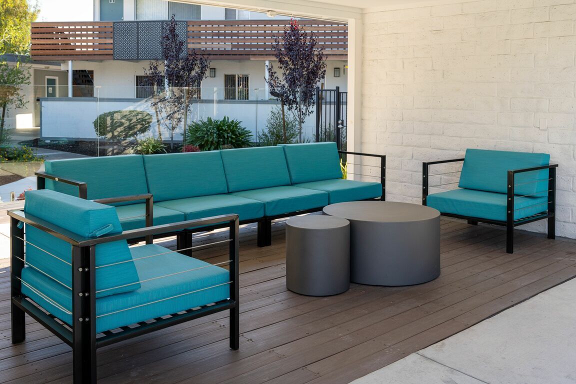 Teal outdoor patio seating set with sofa, chairs, and round gray tables on a wooden deck