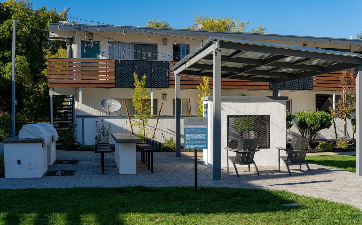 Modern house exterior with balcony, patio seating, and covered carport in daylight
