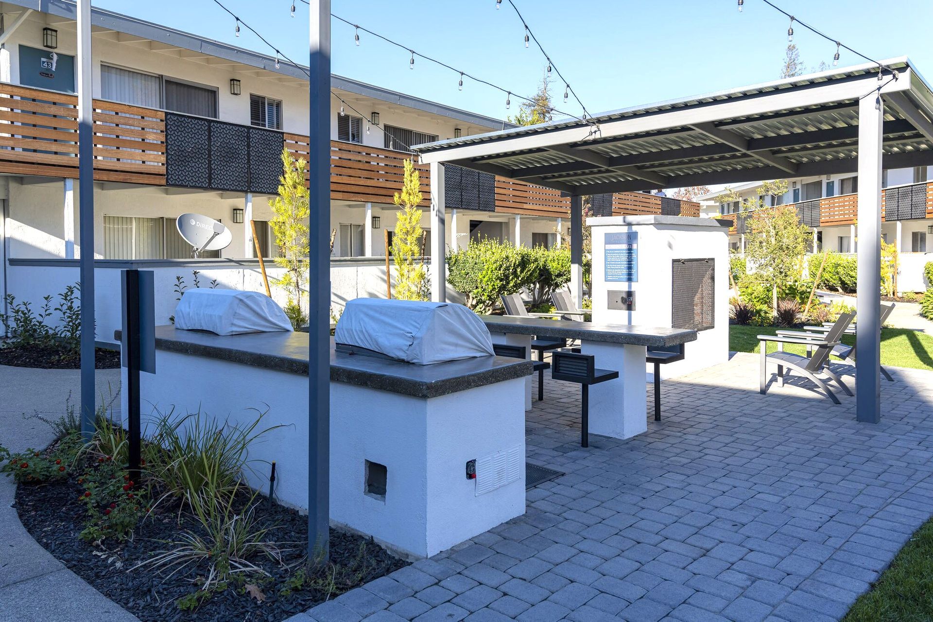 Outdoor patio with picnic tables, white grill covers, and a shaded pergola in a courtyard