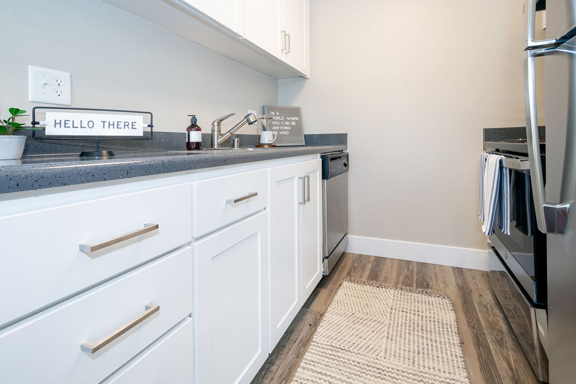 Bright modern kitchen with white cabinets, gray countertops, stainless stove, and a woven runner rug.