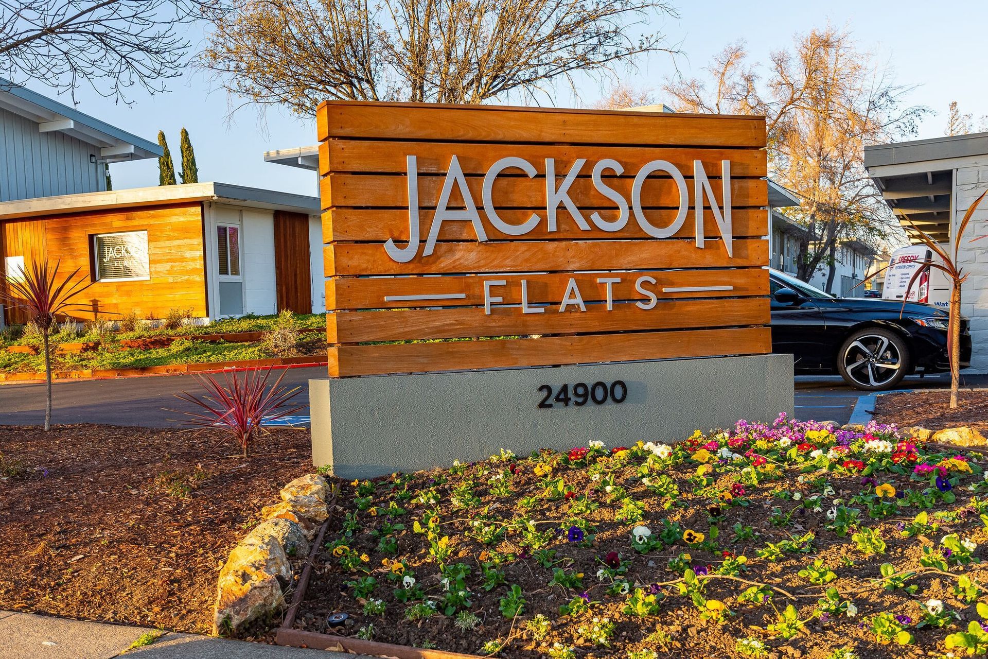 Jackson Flats sign with wood slats, gray base, and colorful flowers in front of apartments