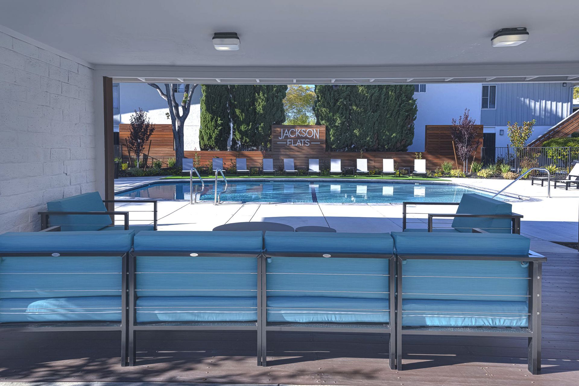 Empty indoor pool with blue lane dividers and lounge chairs, opening to a sunny outdoor patio.