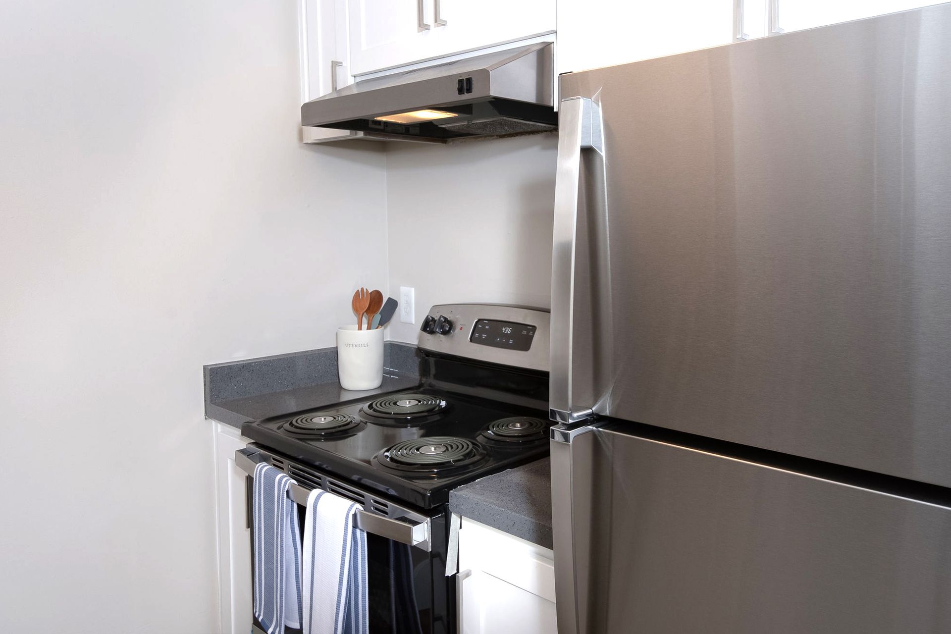 Small modern kitchen with stainless steel refrigerator and stove under a white range hood