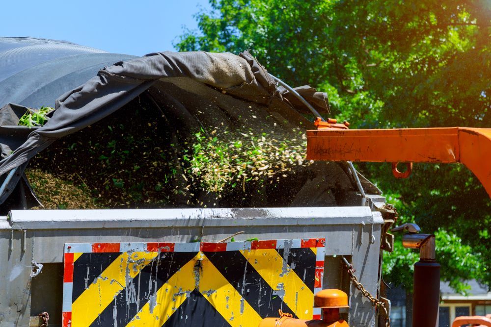 A Man is Standing Next to a Truck That is Being Used to Chop Trees — Tallow Tree Services Pty Ltd in Lennox Head, NSW