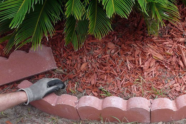 A Person Wearing a Glove is Laying a Brick Edging in a Garden — Tallow Tree Services Pty Ltd in Casino, NSW