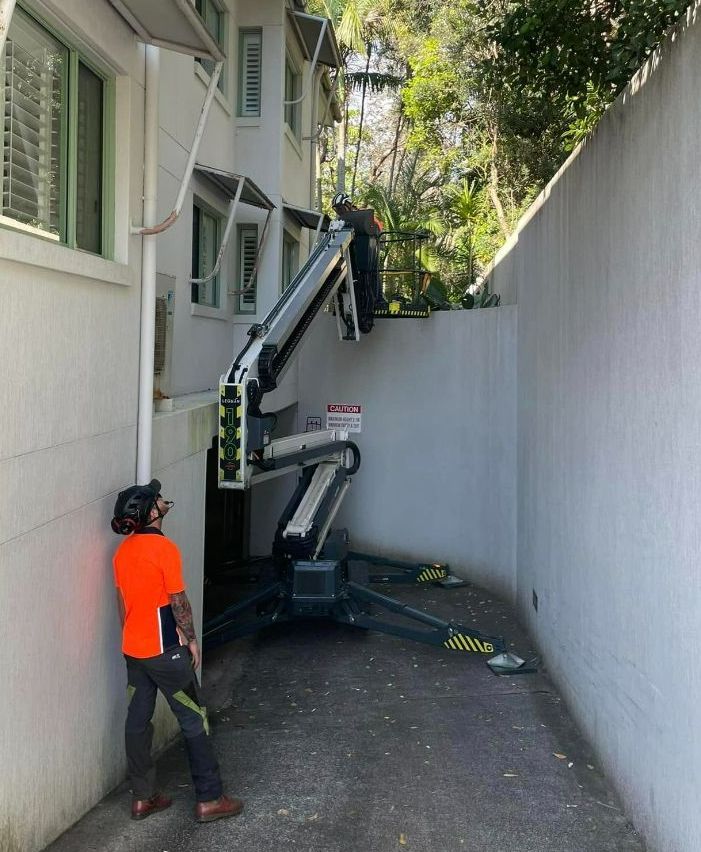 A Man Leaning Against a Wall Next to a Crane — Tallow Tree Services Pty Ltd in Yamba, NSW