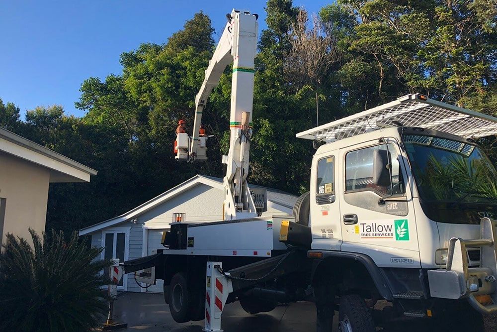 White truck with a crane on top of it is parked in front of a house — Tree Services Byron Bay