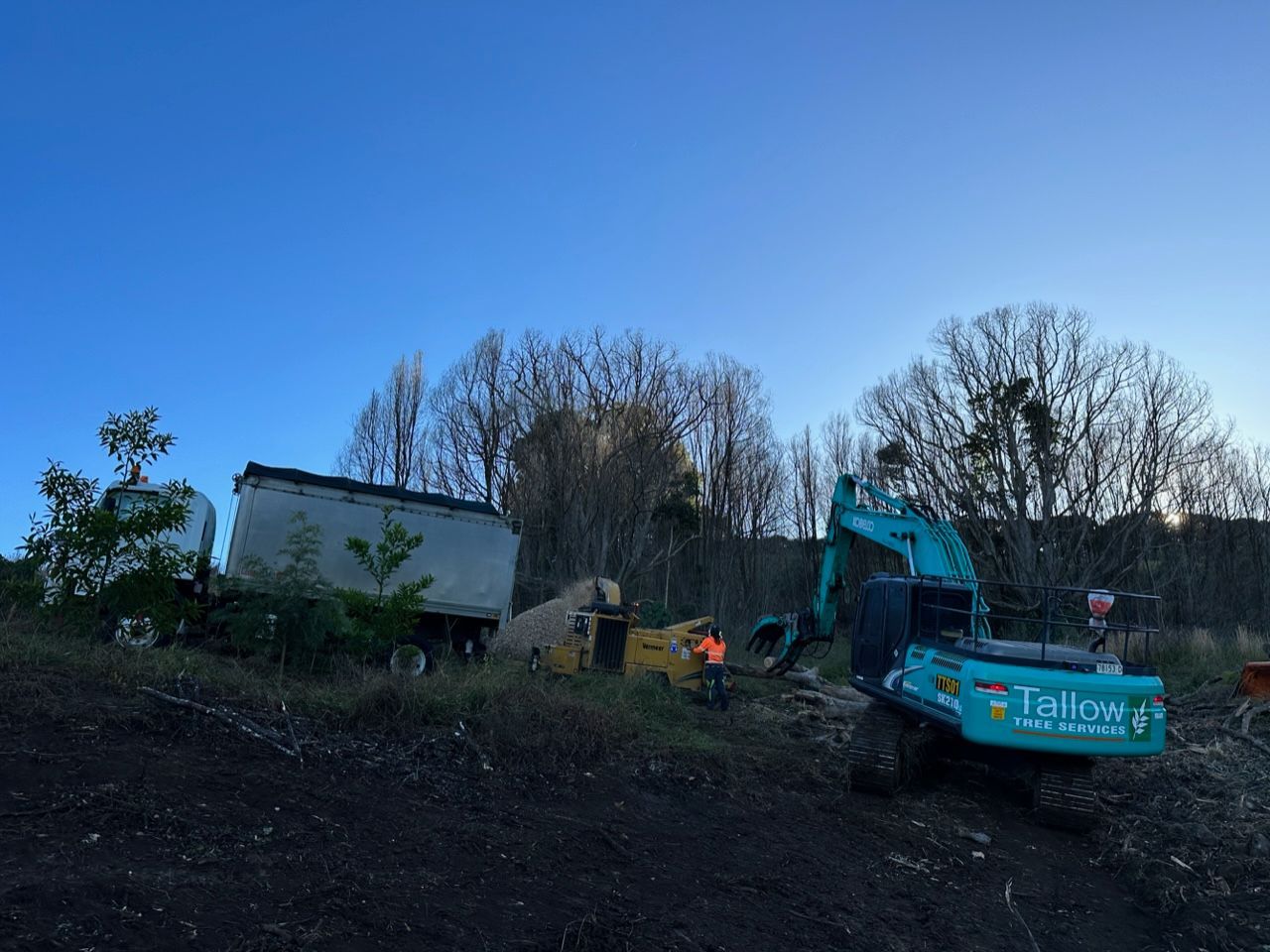 A Blue Excavator is Parked in a Field With Trees in the Background — Tallow Tree Services Pty Ltd in Bangalow, NSW