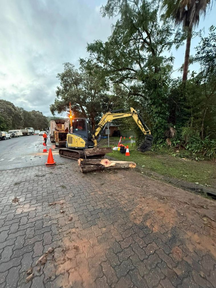 A Yellow Excavator is Sitting on the Side of the Road — Tallow Tree Services Pty Ltd in Mullumbimby, NSW