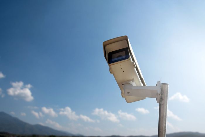 A security camera on a pole with a blue sky in the background.