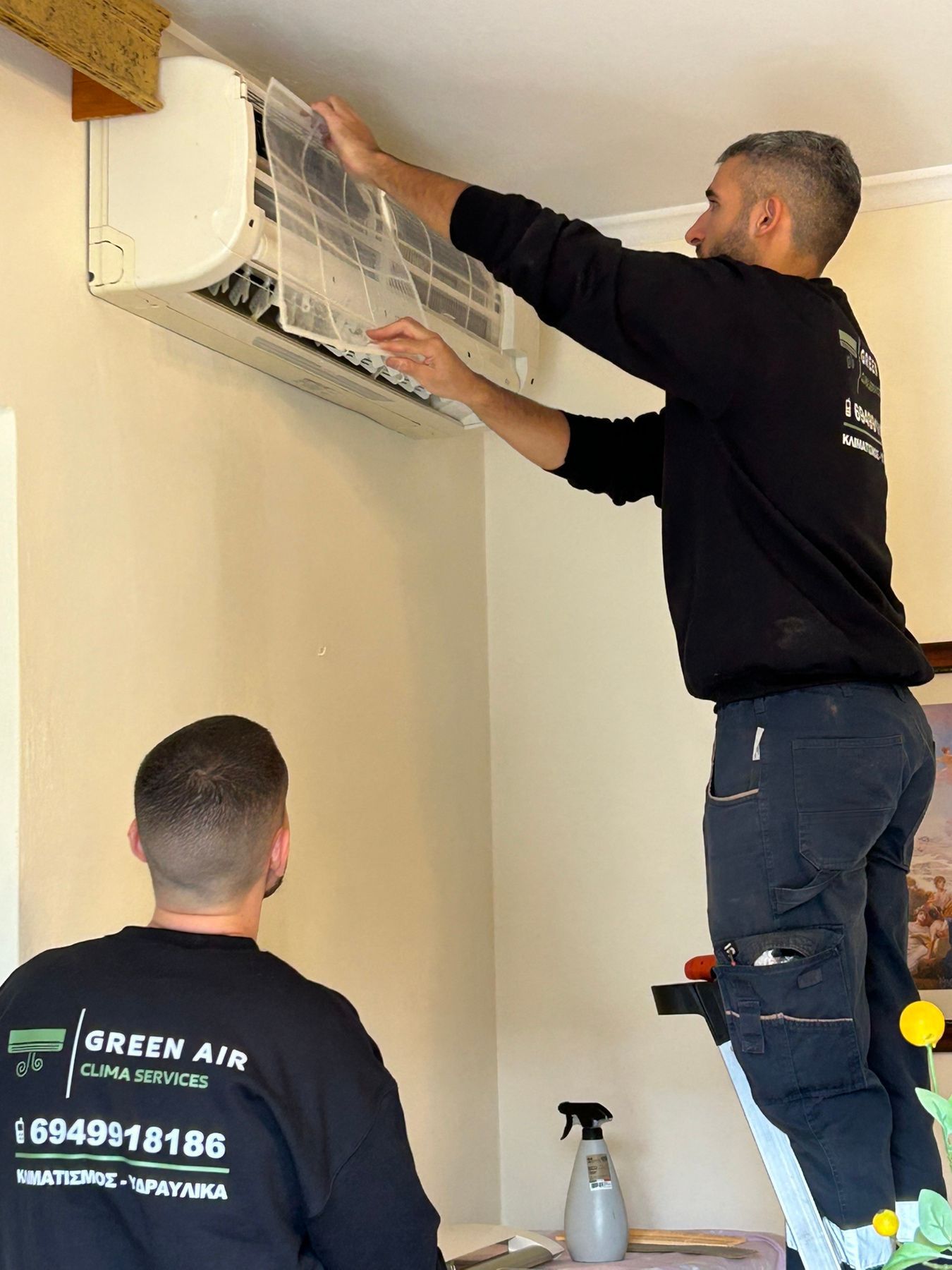 Two HVAC technicians installing a wall-mounted air conditioner indoors.