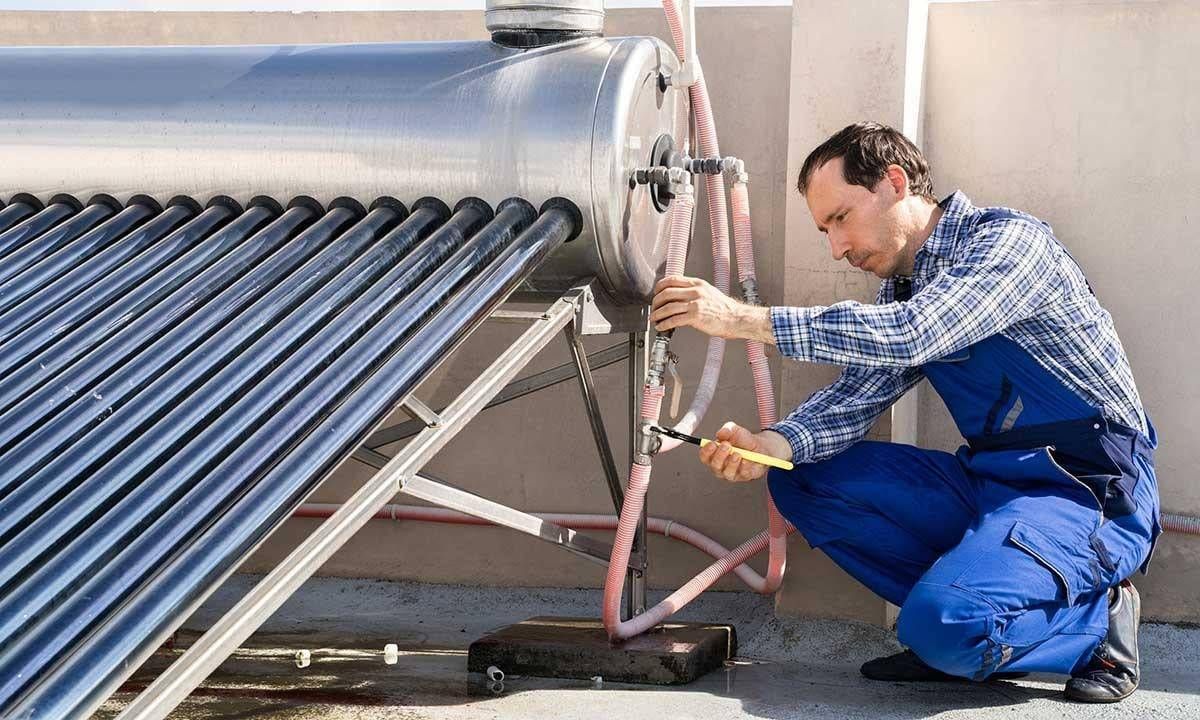 Technician inspecting rooftop solar water heater with vacuum tubes and pipes