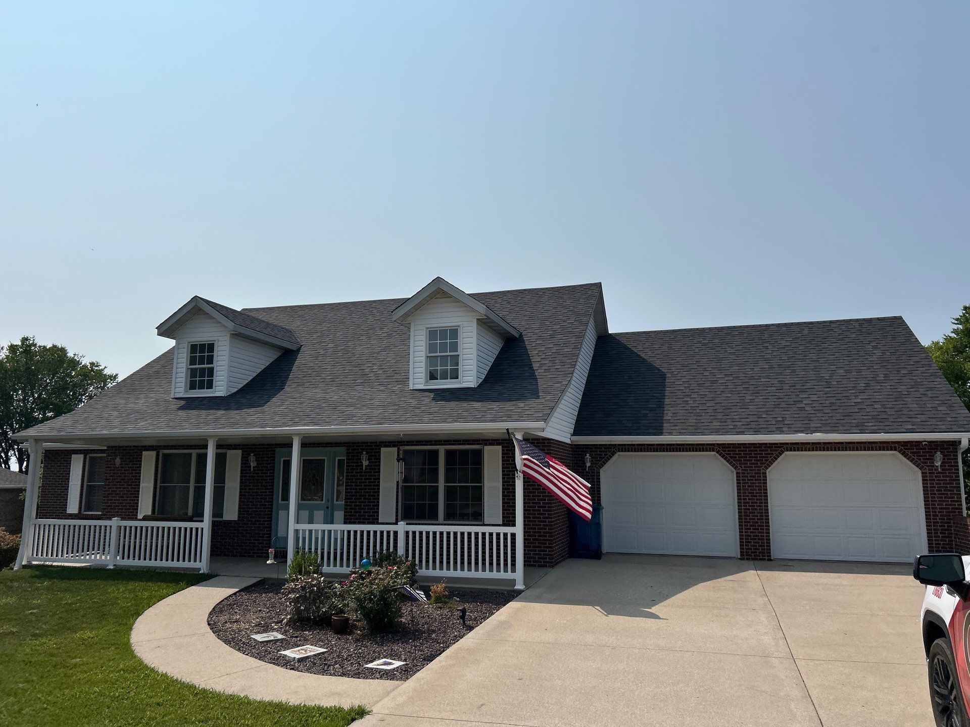 Suburban house with front porch, two-car garage, curved walkway, and an American flag waving by the driveway.