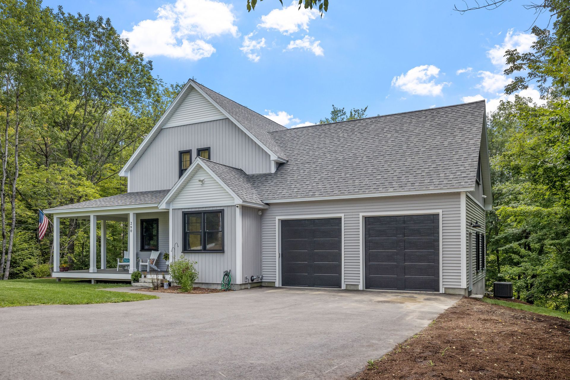 White house with dark gray roof, double garage, and glass front porch in a wooded suburban setting.