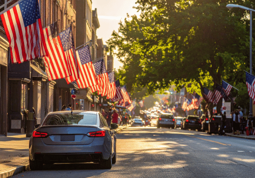 Car driving through downtown street lined with American flags during holiday travel season at sunset