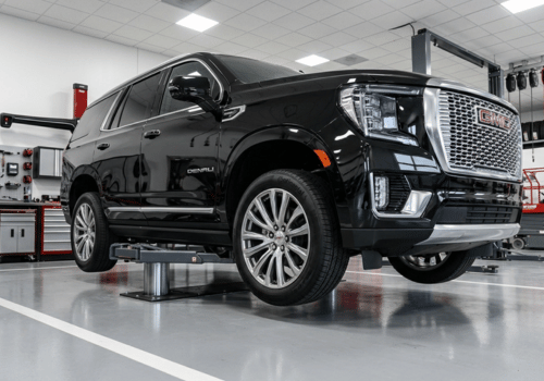 Black GMC Yukon Denali SUV raised on a service lift inside a clean, modern auto repair shop